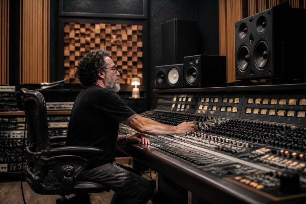 A mastering engineer sitting at a large studio console reviewing waveforms on a high-resolution monitor, surrounded by acoustic panels and professional studio monitors in a treated room