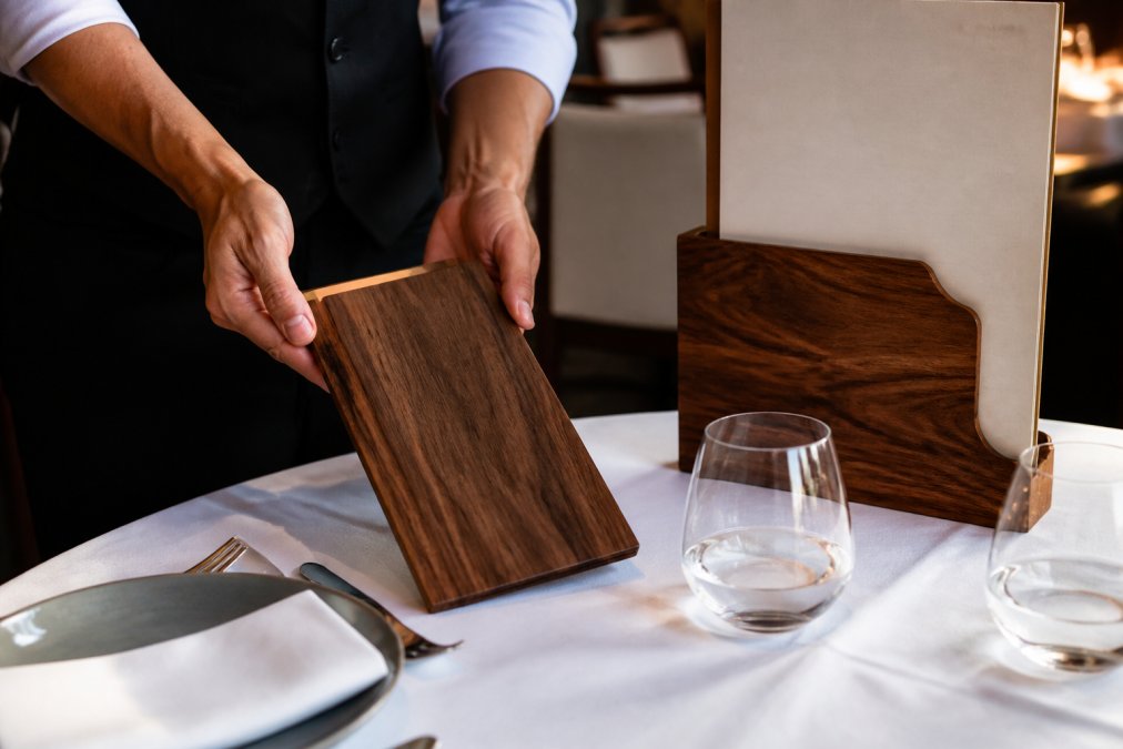 Handcrafted walnut check presenter and logo menu holder on a custom wooden tabletop in a restaurant setting