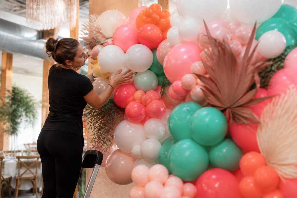 Professional arranging vibrant organic balloon garland with mixed latex balloons in various sizes and colors showing natural asymmetry and texture variation in bright event space