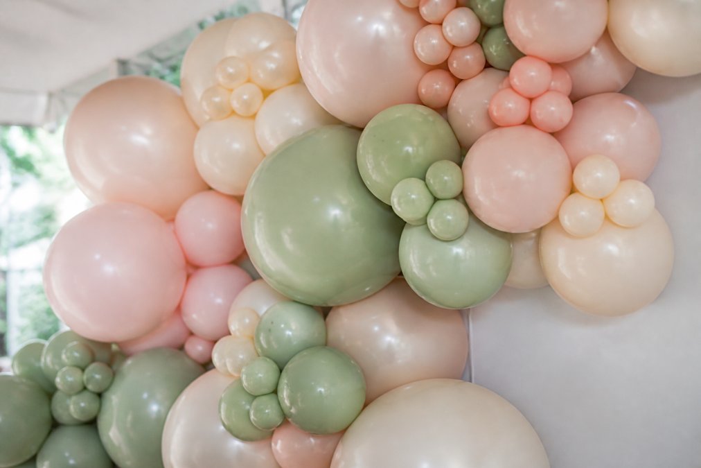 Close-up of professionally arranged organic balloon garland displaying varied latex balloon sizes from small to large, soft matte and pearl finishes in blush, cream, and sage tones, with natural asymmetrical clustering and overlapping balloons creating depth and texture