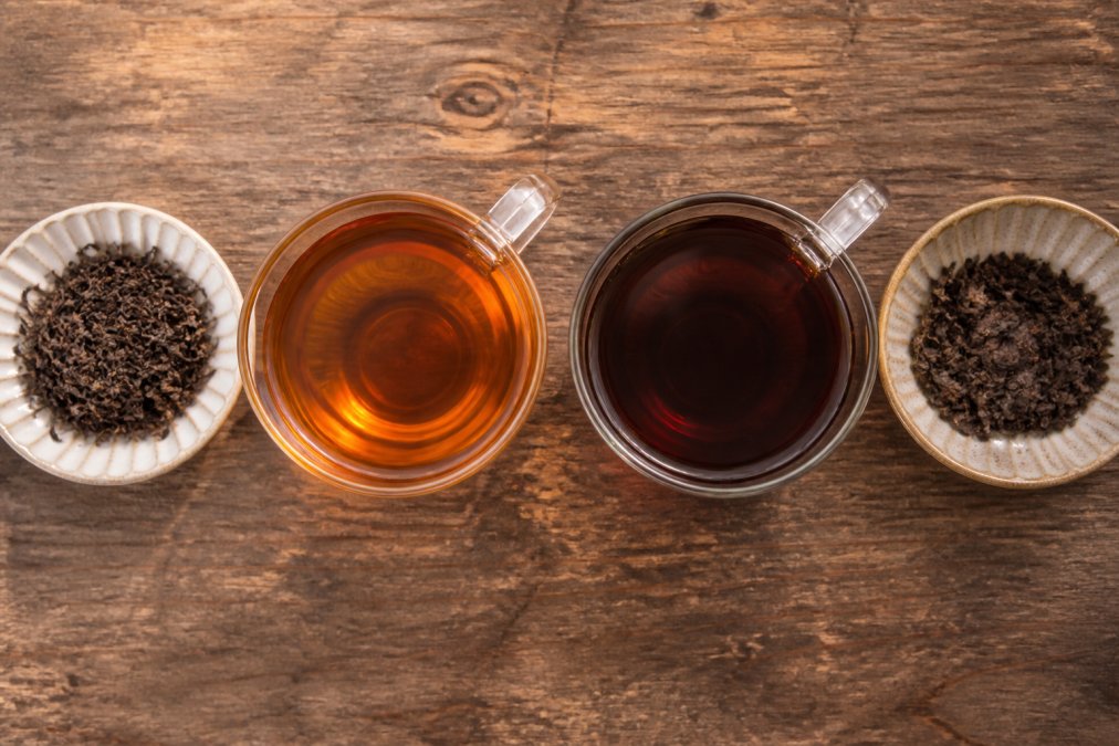 Infographic comparing the flavor profiles and dry leaves of black tea vs pu-erh in glass cups on a wooden table.