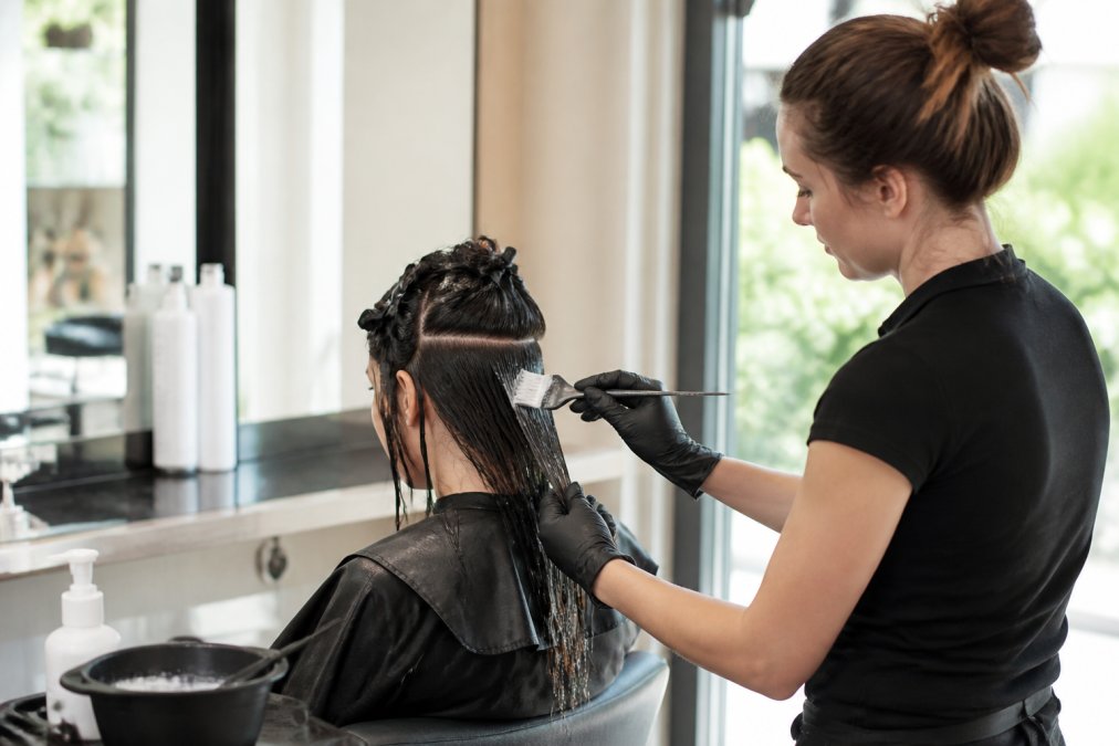 Professional stylist applying organic keratin treatment to sectioned damp hair, working product through strands with precision brush in well-lit salon setting with natural light