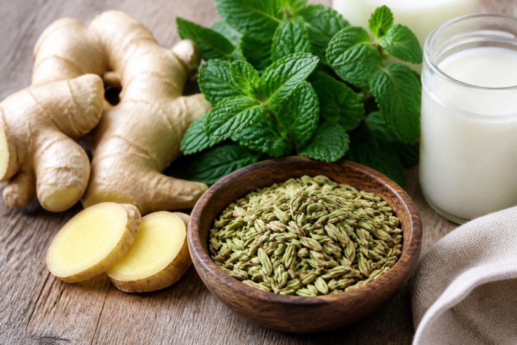 Close-up of fresh ginger root, peppermint leaves, and fennel seeds arranged on a wooden surface with soft natural lighting and organic texture