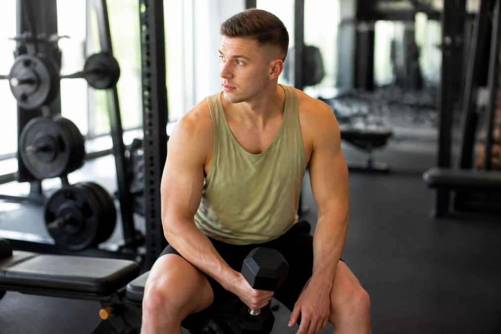 A person in a bright gym setting wearing a soft bamboo-blend singlet, holding a dumbbell between sets, with natural light highlighting the breathable fabric texture