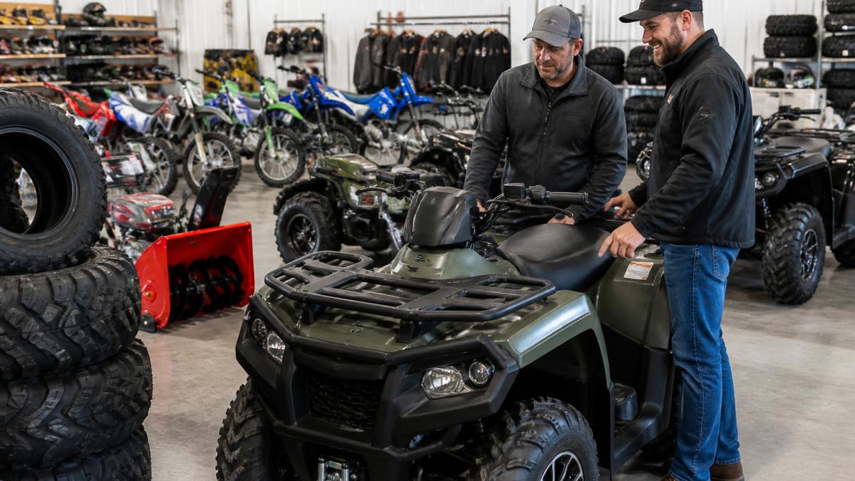 A customer and a friendly salesperson looking at a new ATV inside a bright showroom, with rows of ATVs and dirt bikes visible in the background