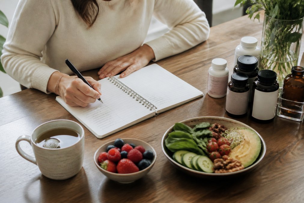 Iemand houdt een dagboek bij over welzijn en voeding naast orthomoleculaire supplementen, thee en gezonde hapjes op een