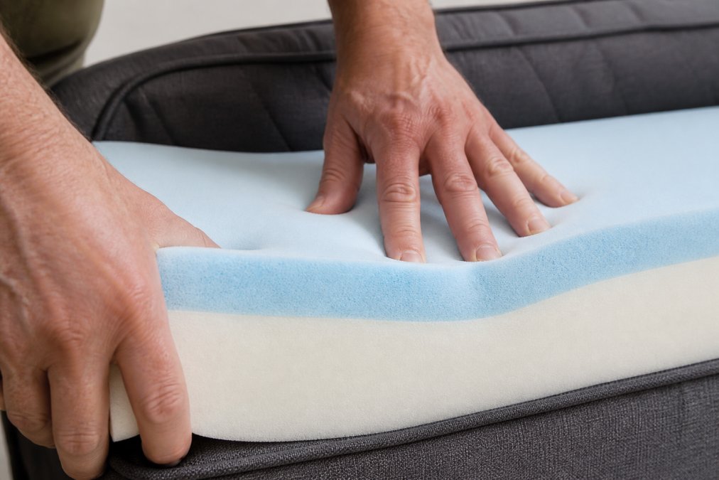 Close-up of hands pressing into an orthopedic dog bed foam to demonstrate cushioning depth and material density, showing finger indentation and foam recovery