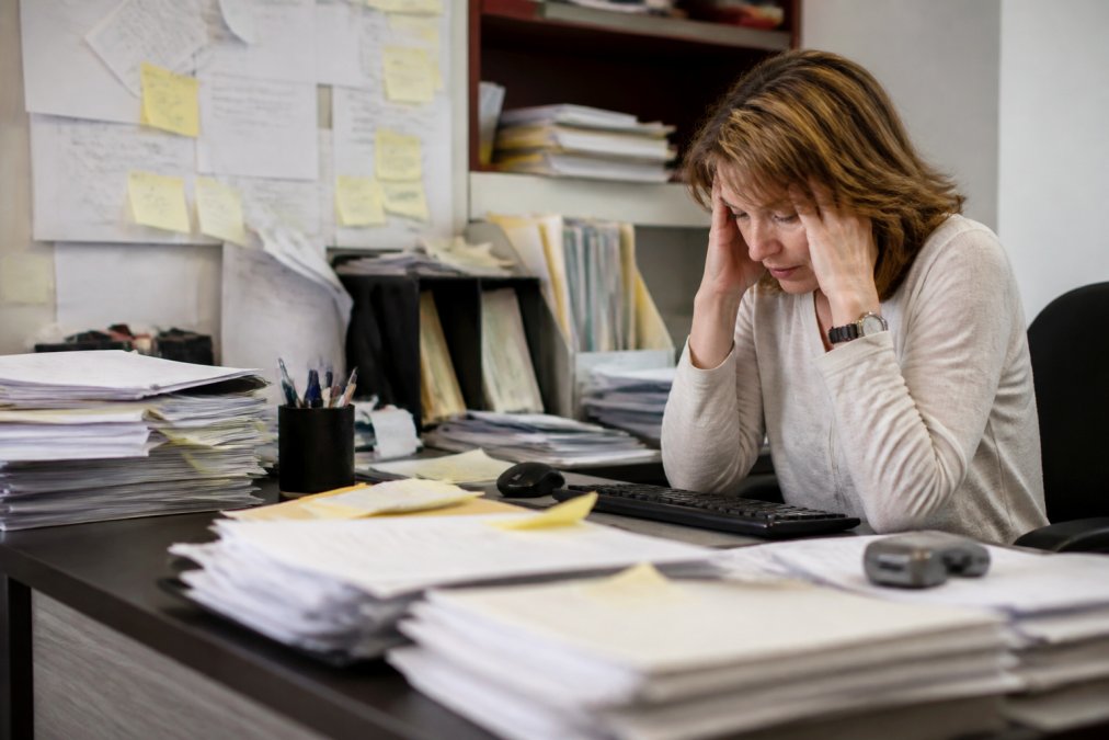 Stressed practice manager buried in paperwork while managing credentialing tasks in a small clinic office