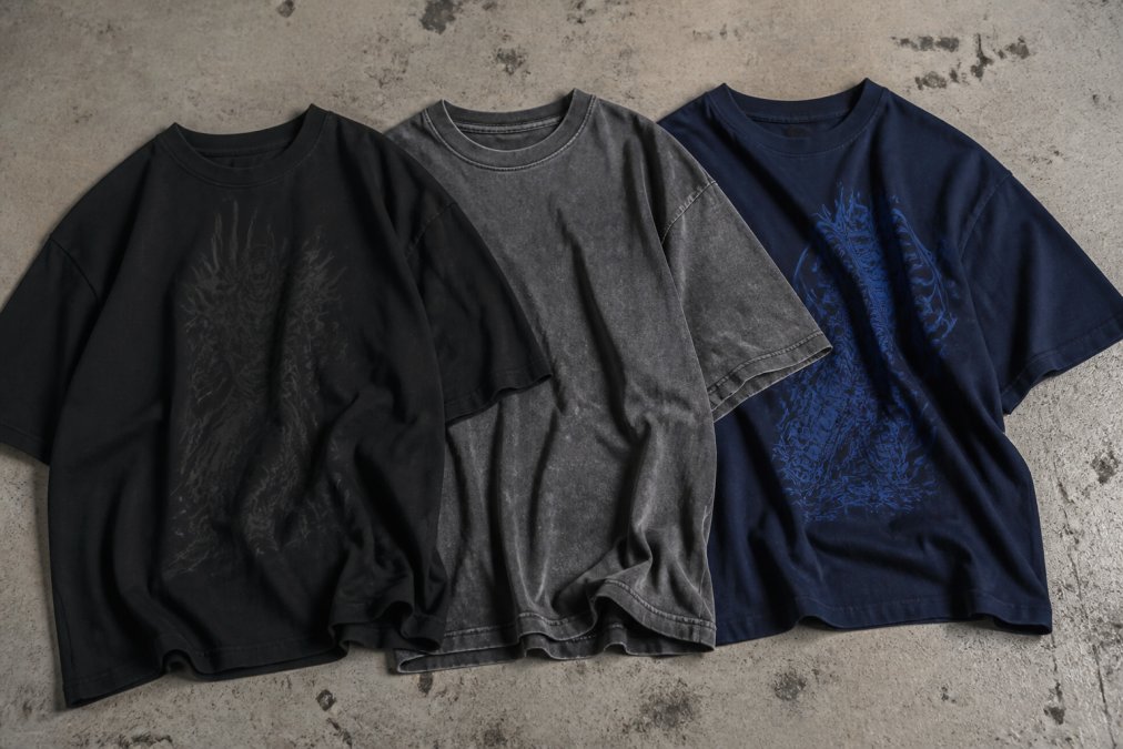Close-up van drie oversized gaming-T-shirts in complementaire kleuren: zwart met subtiele graphic, donkergrijs met een vervaagd effect en donkerblauw met print, naast elkaar gerangschikt op een vlakke ondergrond, met duidelijk zichtbare textuur en pasvorm