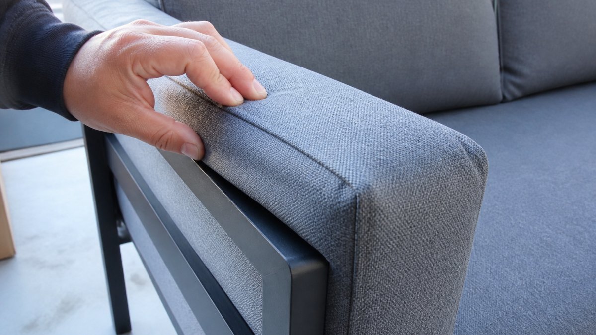 Close-up of furniture piece being inspected by hand, showing fabric texture and frame details in natural daylight