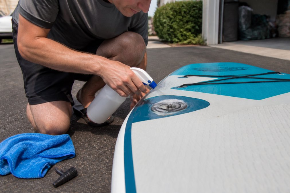 Person spraying soapy water on a paddleboard losing air to find a leak