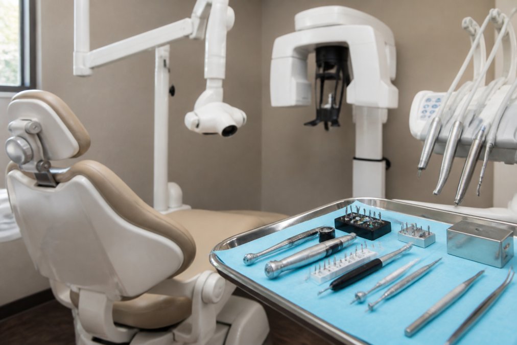 Modern dental operatory with digital imaging equipment mounted on arm, 3D cone beam scanner visible in background, rotary instrumentation tools arranged on stainless steel tray under bright clinical overhead lighting