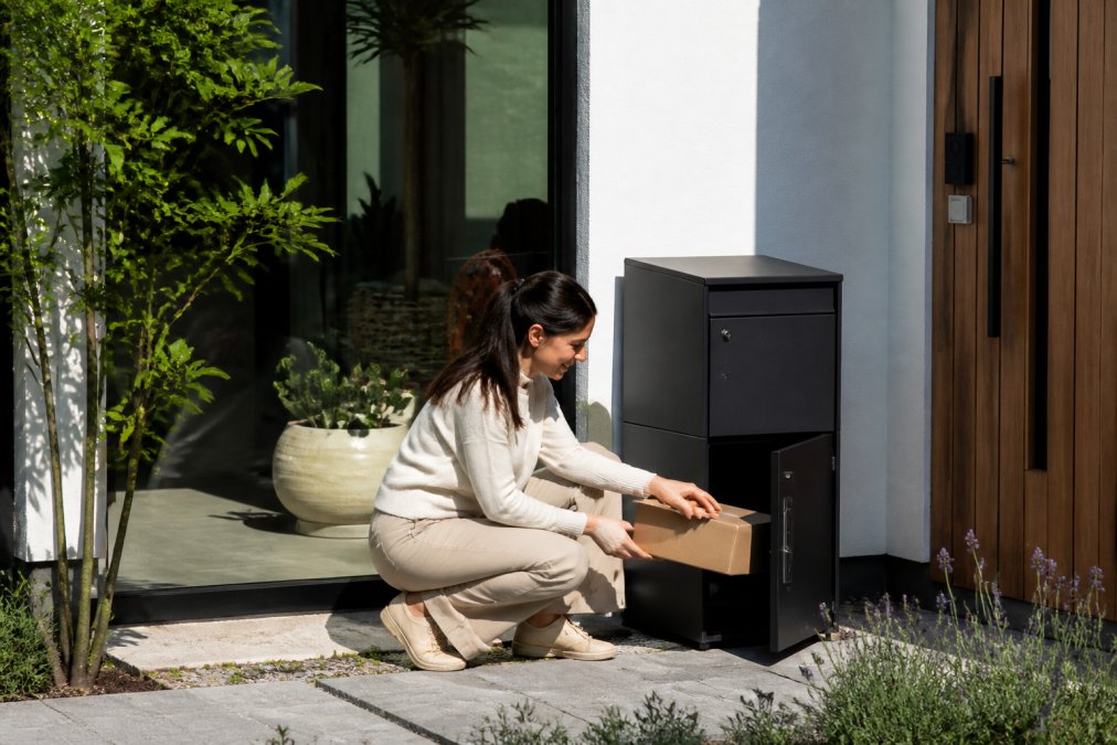 Huiseigenaar haalt pakket uit luxe pakketbrievenbus bij voordeur op zonnige dag, stijlvolle woning op achtergrond, natuurlijk daglicht
