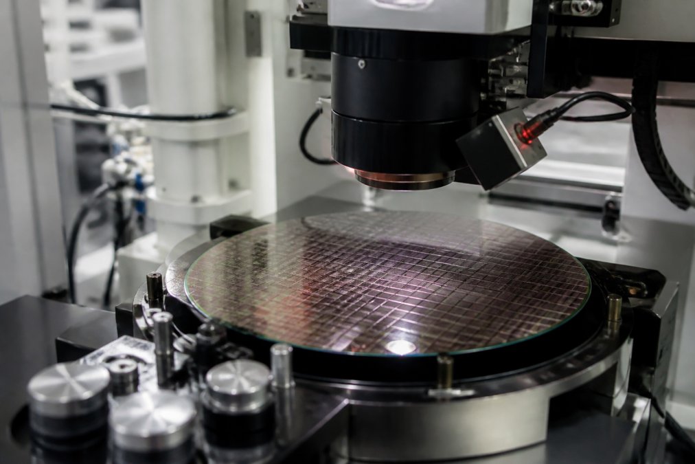 Close-up of a 300mm wafer positioned on a precision inspection platform with advanced optical detection sensors and measurement equipment positioned above in a controlled cleanroom environment