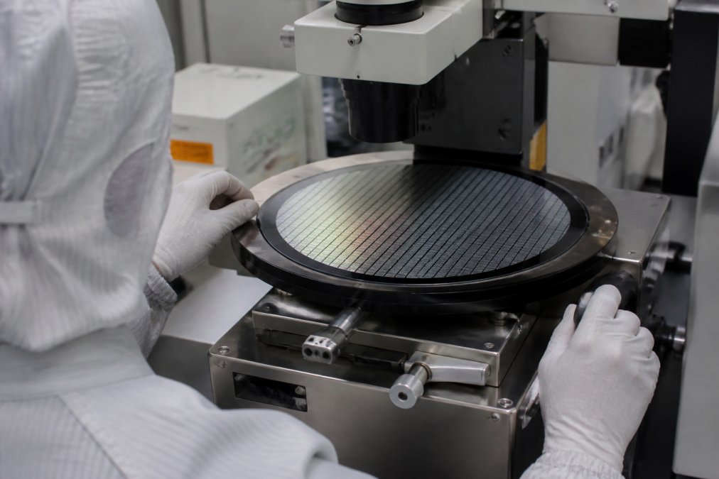 Semiconductor wafer under electron beam inspection equipment with technician monitoring real-time metrology data on multiple screens in a cleanroom environment