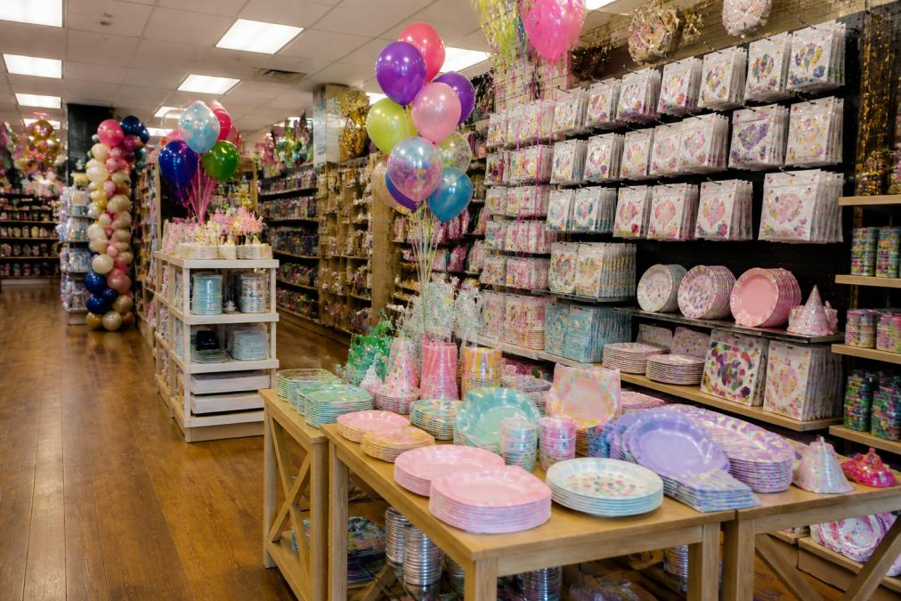 Bright, welcoming party store interior with colorful displays of themed decorations, balloons, tableware, and party favors organized on shelves and tables