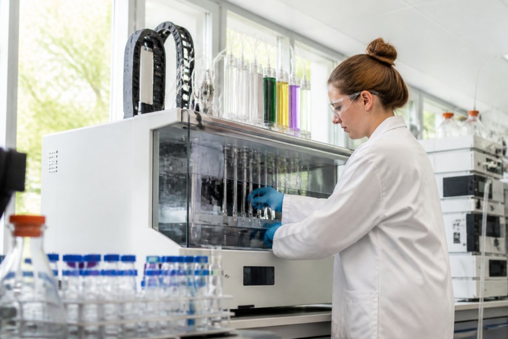 Onderzoeker werkend met geautomatiseerde peptidesynthesizer in modern laboratorium, met gekleurde displays en precisie-instrumenten zichtbaar in natuurlijk licht
