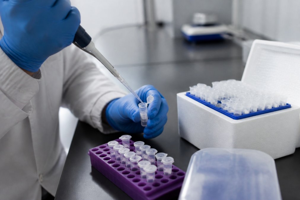 A gloved researcher using a precision pipette to transfer a peptide solution into a small cryogenic vial on a laboratory bench, with a rack of labeled vials nearby