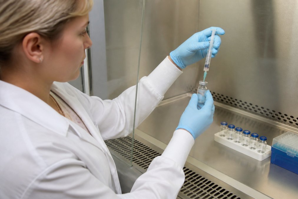 Laboratory technician using sterile technique to reconstitute a peptide vial with bacteriostatic water and syringe, wearing gloves in a controlled lab environment