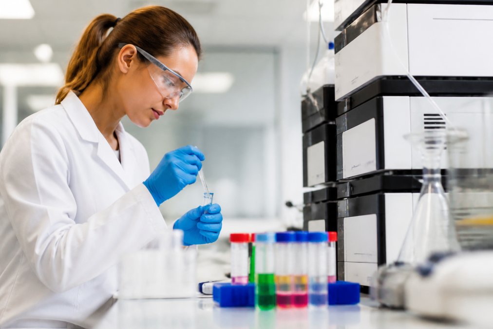 Laboratoriumtechnicus die voorzichtig een peptide-monster voorbereidt voor HPLC-analyse, met gekleurde testbuizen en meetapparatuur op de werkbank onder helder laboratoriumlicht