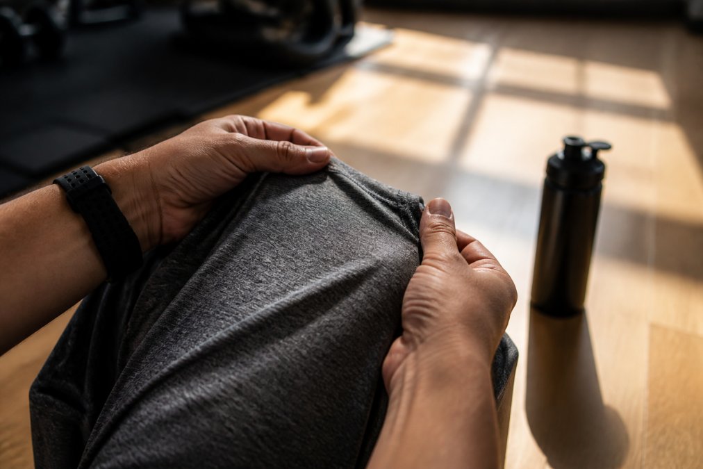Hands feeling the soft, breathable fabric of a performance shirt in a sunlit gym with a water bottle nearby