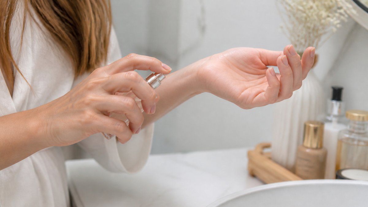 Close-up of a woman's wrist and inner forearm as she gently dabs perfume from a small glass bottle, soft natural light, clean minimal bathroom setting, focus on the delicate skin and careful motion