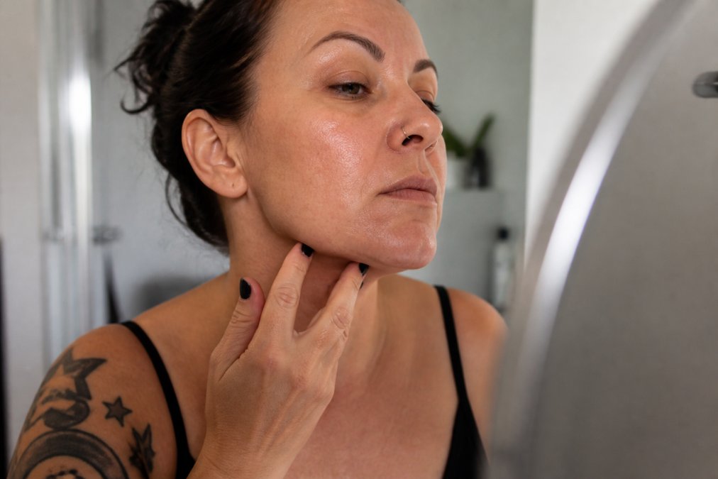 Close-up of a woman's face showing textured skin along the jawline and chin area, natural lighting, no makeup, honest and relatable expression with slight concern