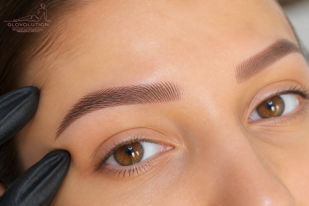 Close-up of a woman's eyebrows showing naturally feathered nano brow strokes with soft, defined hair-like lines and proper color saturation under professional lighting