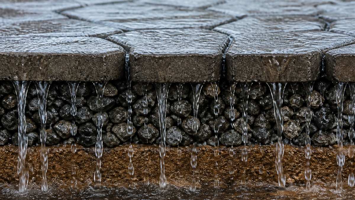Diagram showing how permeable driveway solutions drain stormwater through pavers into the aggregate base.