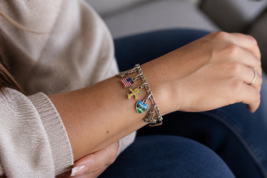 A wrist wearing a bracelet with personalized charms for military family milestones in soft natural light.