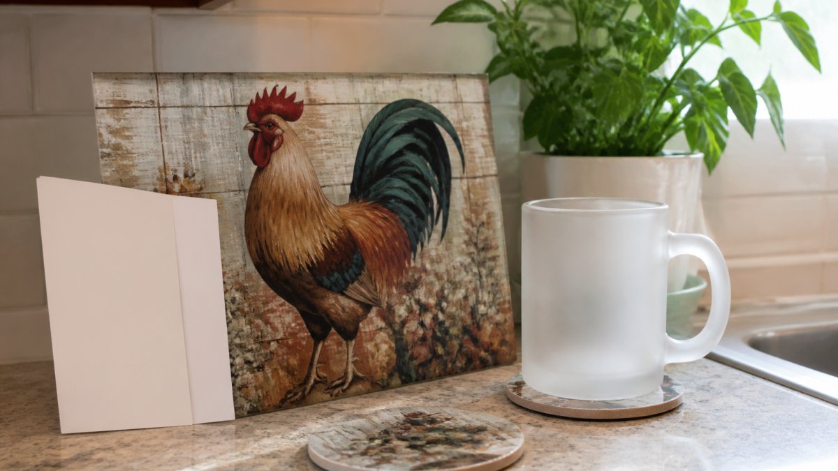 A bright kitchen counter styled with a farmhouse rooster glass cutting board, a frosted glass mug, and ceramic coasters, with a housewarming card leaning against the board