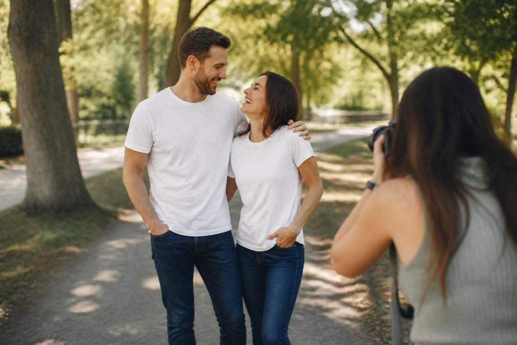 A happy couple wearing matching shirts saying Est. 2016 laughing together during a sunlit anniversary photoshoot.