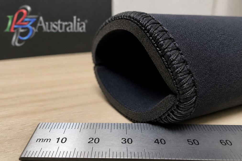 Close-up of neoprene stubby holder seam detail showing reinforced stitching and material thickness, with a ruler or scale indicator for reference
