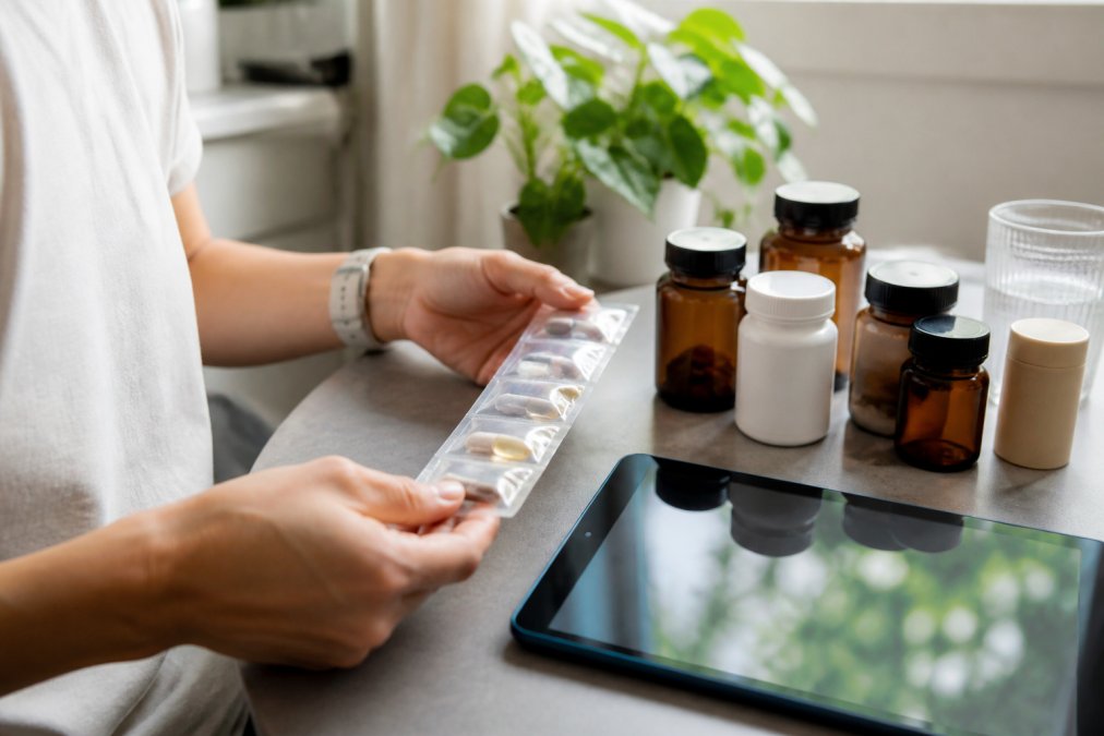 Hands holding a personalised supplement routine with bottles arranged on a clean surface, with a digital health report displayed on a tablet showing genetic insights and recommendations nearby