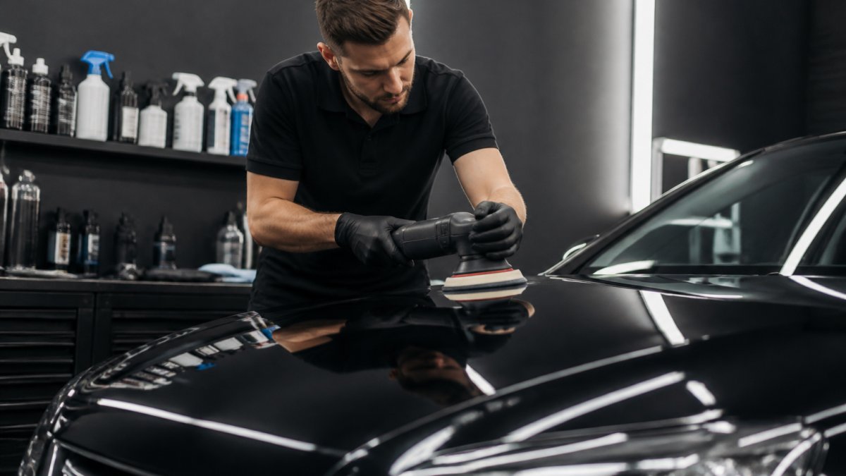 Professional detailer aan het werk: handen polijsten een autolak met concentratie op het glanzende oppervlak, professionele werkomgeving met detailingproducten zichtbaar in de achtergrond