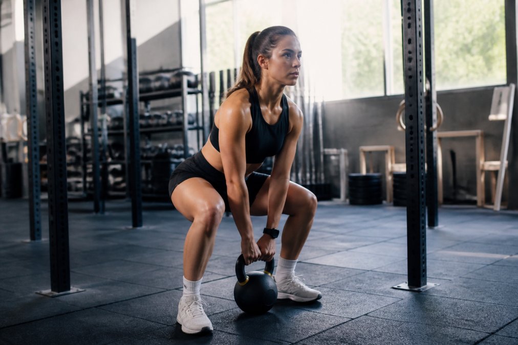 An athlete in performance activewear doing a strength and conditioning workout in a well-lit gym, expression focused and determined