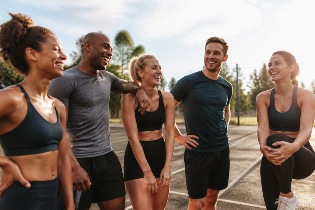 A diverse group of athletes wearing athletic apparel gathered together after a training session, smiling and showing community spirit in a bright outdoor setting with warm natural light