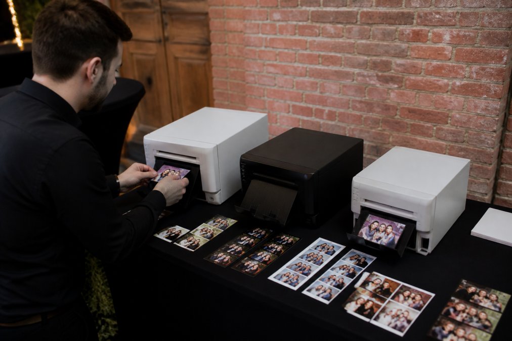 Drie verschillende professionele dye-sublimatieprinters naast elkaar op een evenementtafel, met geprinte fotoseries ernaast en een operator die een foto in de printer plaatst
