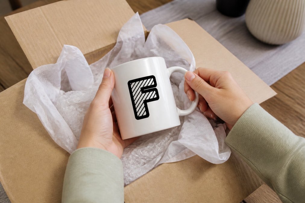 Hands carefully unboxing a personalized ceramic mug with secure protective wrapping and tissue paper, showing the vibrant custom design clearly visible on the glossy white mug
