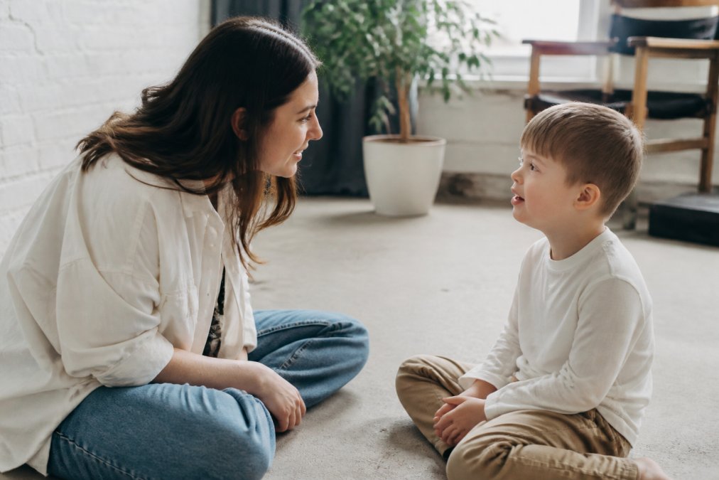 Professional photographer having a calm, one-on-one conversation with a young child in a quiet, softly lit studio space before the session begins, showing genuine connection and reassurance