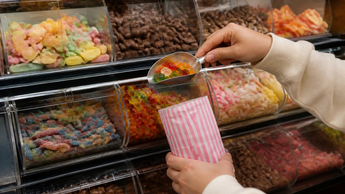 Close-up of hands selecting colourful sweets from shelves, showing the variety of gummies, chocolates, and retro treats available in a pick and mix selection