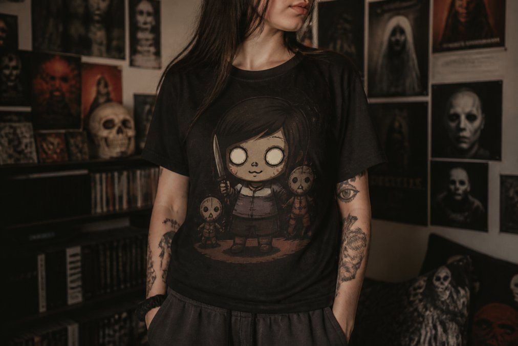 A person wearing a dark graphic t-shirt featuring a creepy-cute cartoon character, standing in a dimly lit room with horror movie posters on the wall