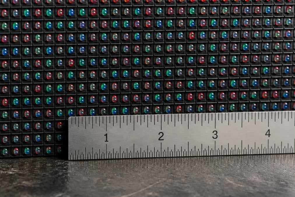 Close-up van de achterzijde van een LED-paneel waarop de rijen rode, groene en blauwe lampjes zichtbaar zijn naast een meetlat in millimeters