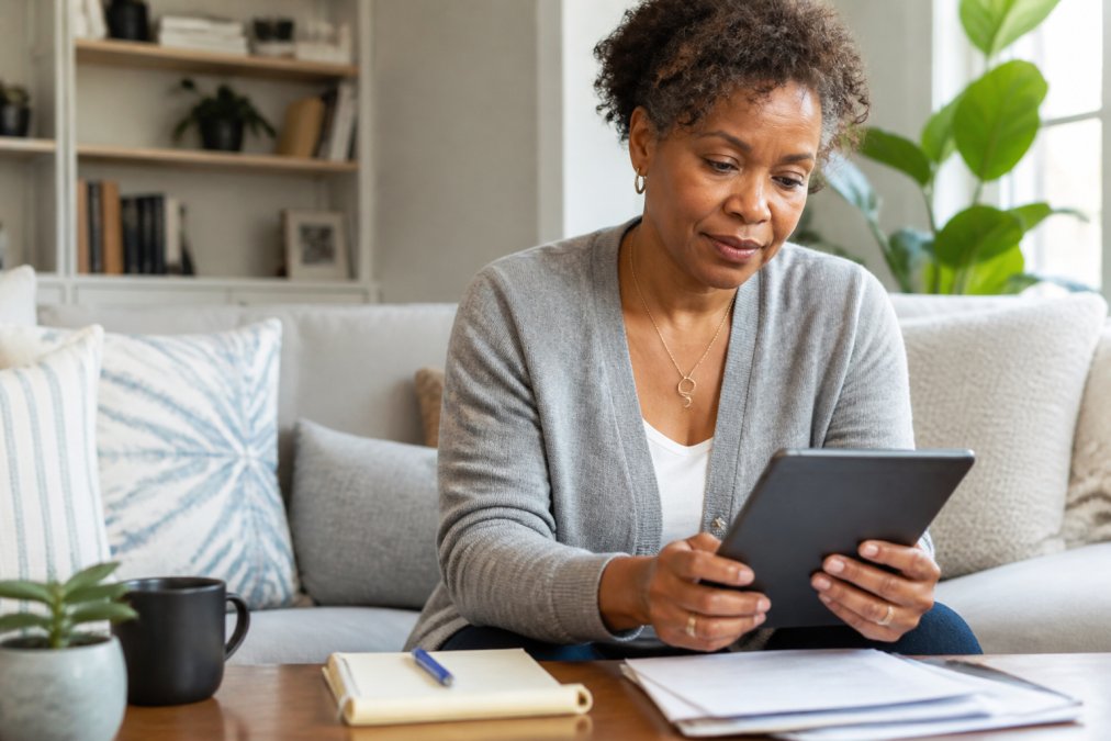 Woman reviewing plain language health insurance documents on a tablet at home while taking notes