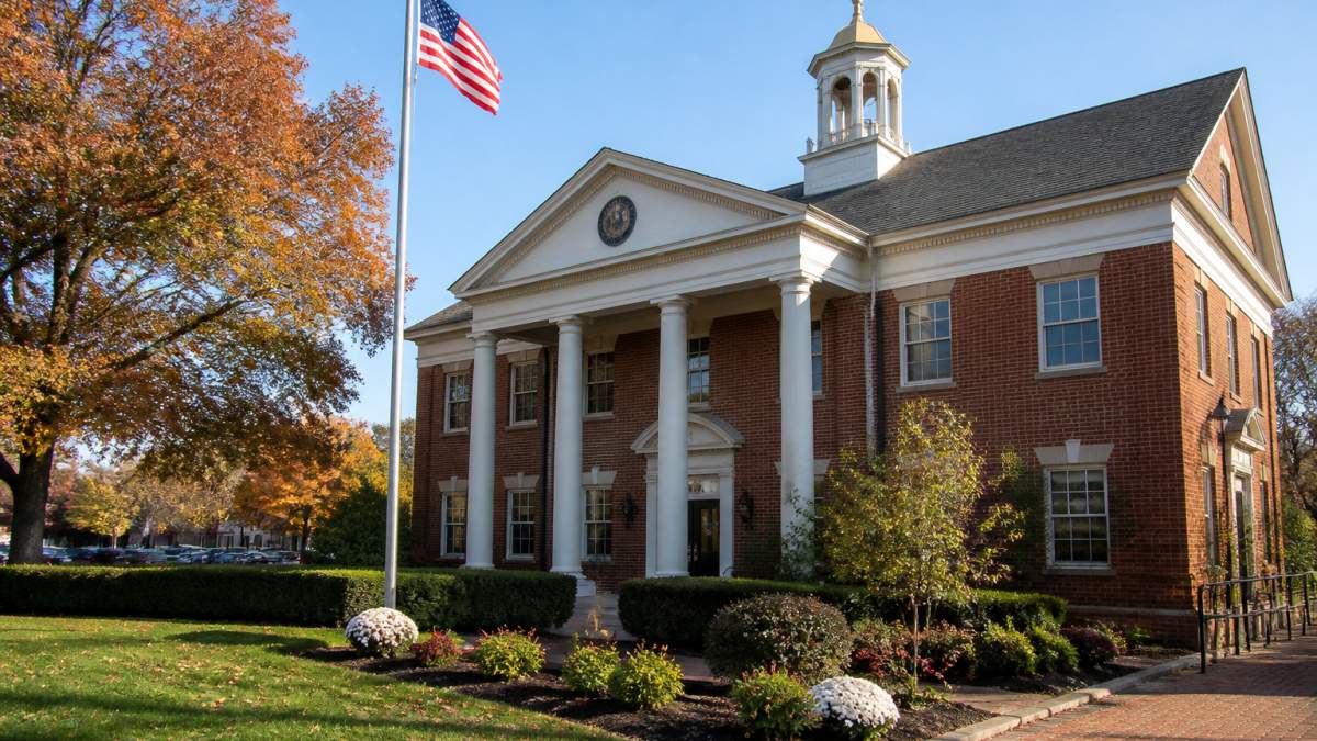 Town hall building with American flag and municipal signage on a clear autumn morning, with manicured landscaping and brick architecture