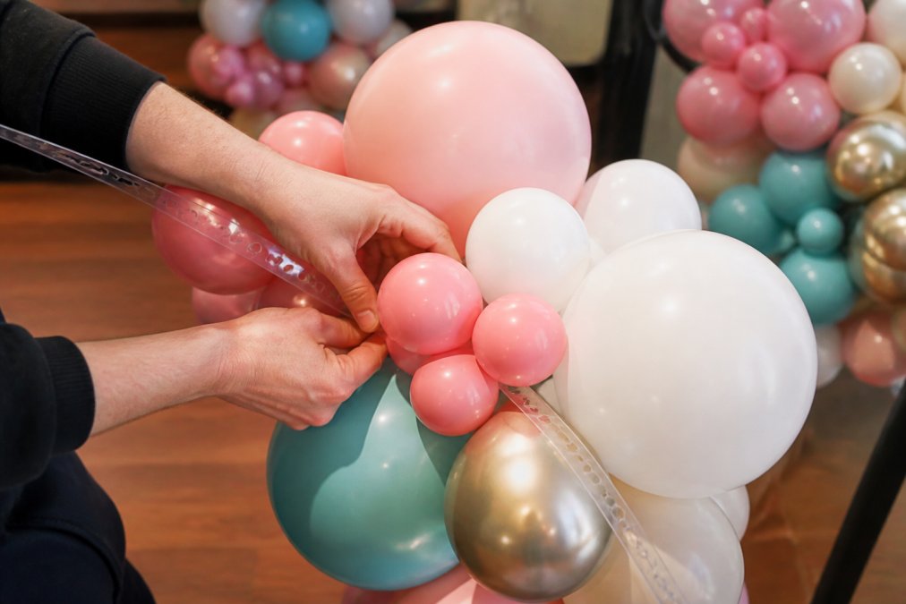 Close-up of hands arranging colorful latex balloons on a balloon strip, showing the clustering technique with various balloon sizes and textures