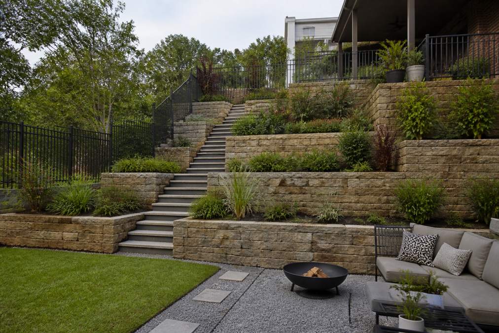 Completed tiered garden on a steep hillside showing multiple retaining walls, level outdoor living areas, garden stairs connecting the tiers, and established plantings on each level
