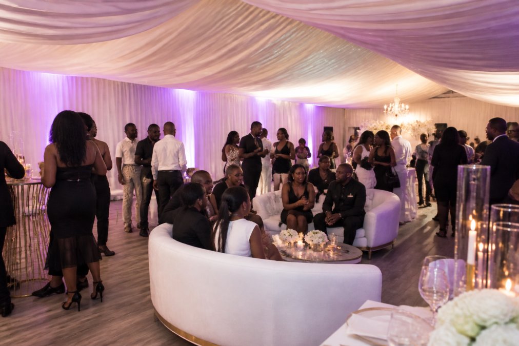 Elegantly decorated event space with soft up-lighting, lounge furniture, and draped ceilings, showing guests mingling at a well-styled intimate gathering
