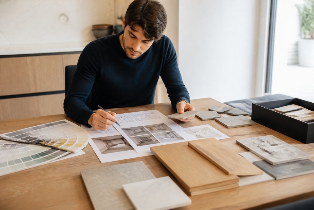 Huiseigenaar bekijkt materiaalmonsters en moodboards voor de planning badkamer en keuken renovatie aan een houten tafel.