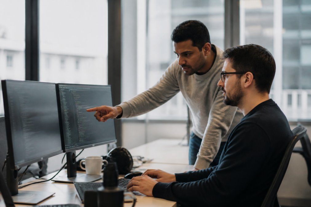 Security engineer and colleague reviewing policy code for ai agent control on dual monitors in a modern office